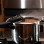 Steam escaping from lid of pressure cooker with reflection of modern kitchen