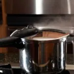 Steam escaping from lid of pressure cooker with reflection of modern kitchen