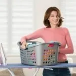 Smiling Young Woman With Iron And Basket Full Of Clothes