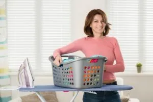 Smiling Young Woman With Iron And Basket Full Of Clothes